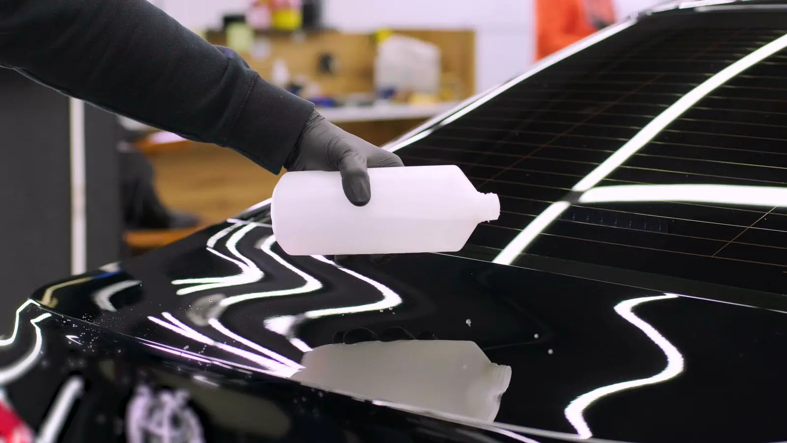 Detailer applying a coating product to glossy black paintwork in the shop