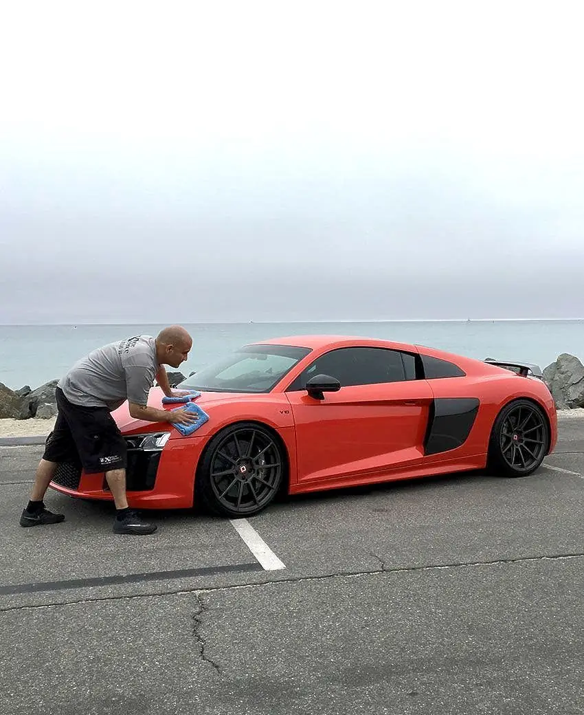 Detailer hand-drying a red Audi R8 by the Orange County coast
