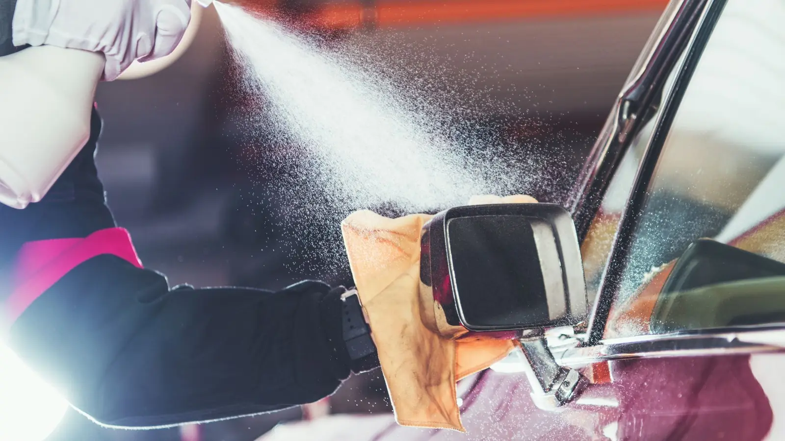 Gloved detailer spraying and wiping down a vehicle mirror during a full detail