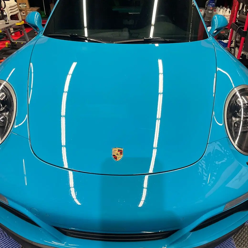 Miami blue Porsche 911 hood reflecting shop lights after polishing
