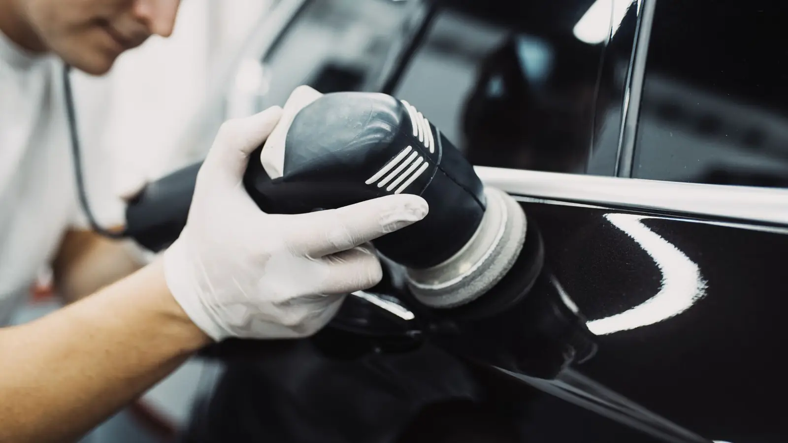 Gloved detailer machine polishing a black panel to a mirror finish