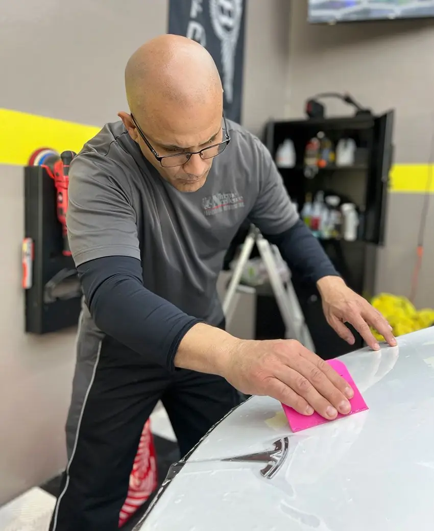 Detailer smoothing paint protection film onto a white hood