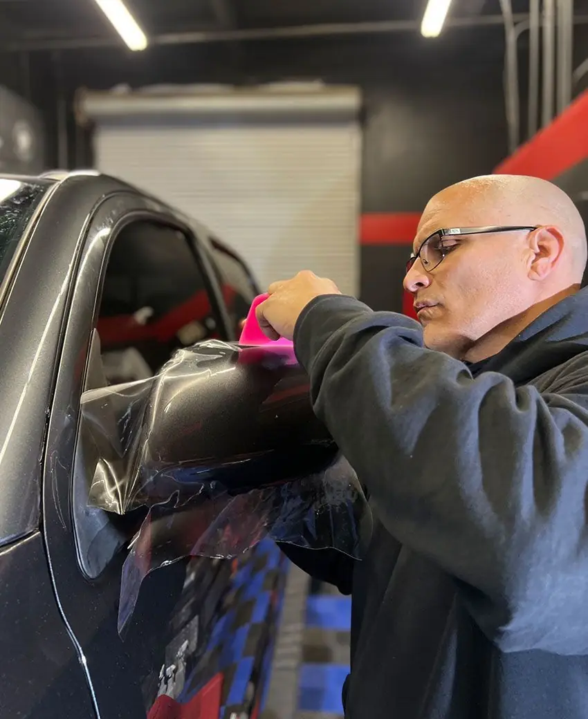 Detailer squeegeeing paint protection film onto a dark fender